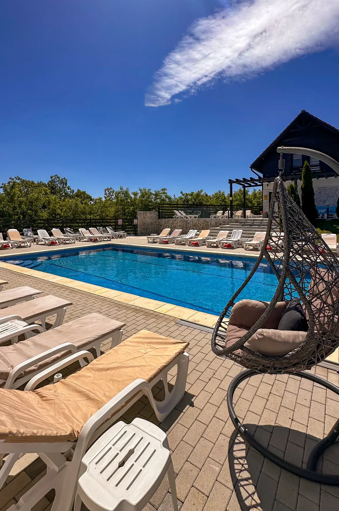 Șezlonguri și balansoar lângă piscina exterioară